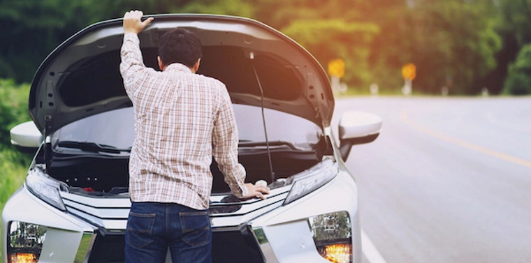 Man looking under the bonnet of a broken down car at roadside.