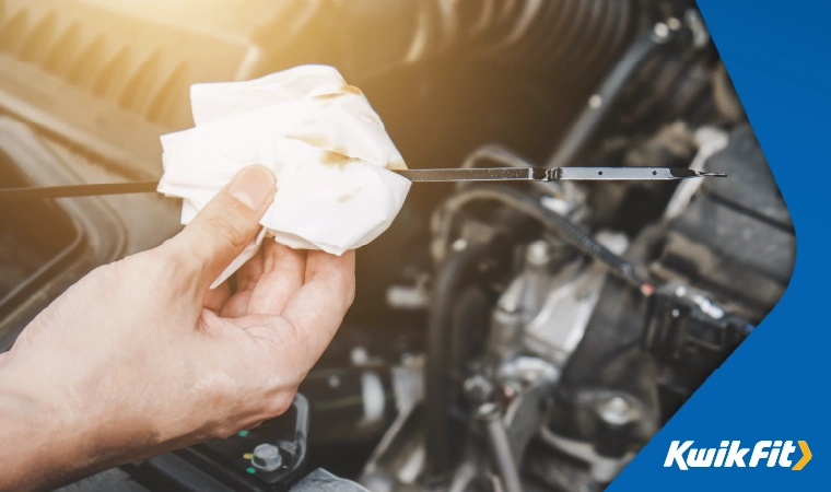 A person uses a tissue and dipstick to check the oil level in their car.