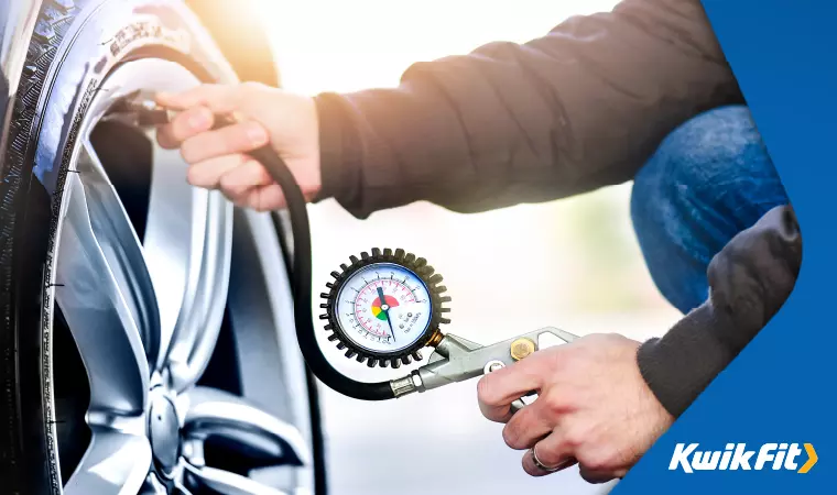 A driver checks their tyre pressure using a dial gauge to ensure it is within the correct bounds.