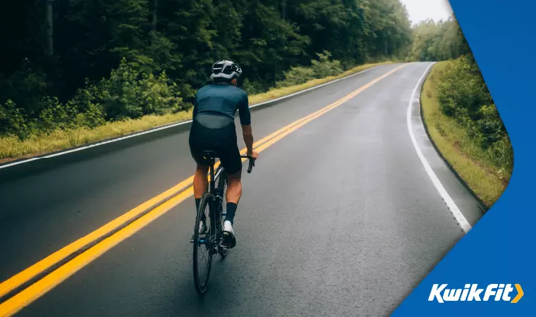 Cyclist rides on a road through lush trees.