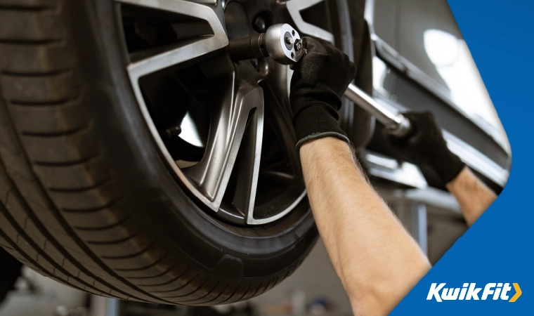 Technician tightening wheel nuts with a silver wrench.