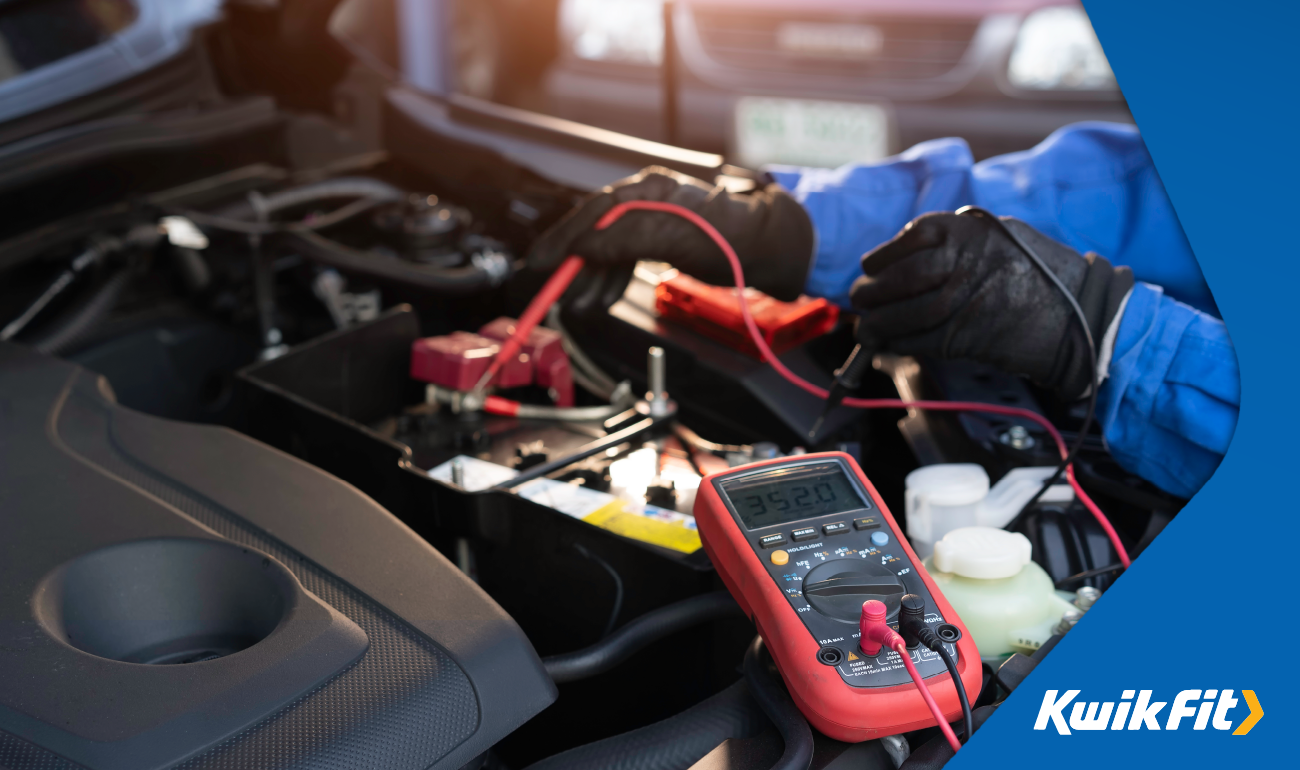 Technicians with blue boiler suits and black gloves testing the battery of a vehicle.