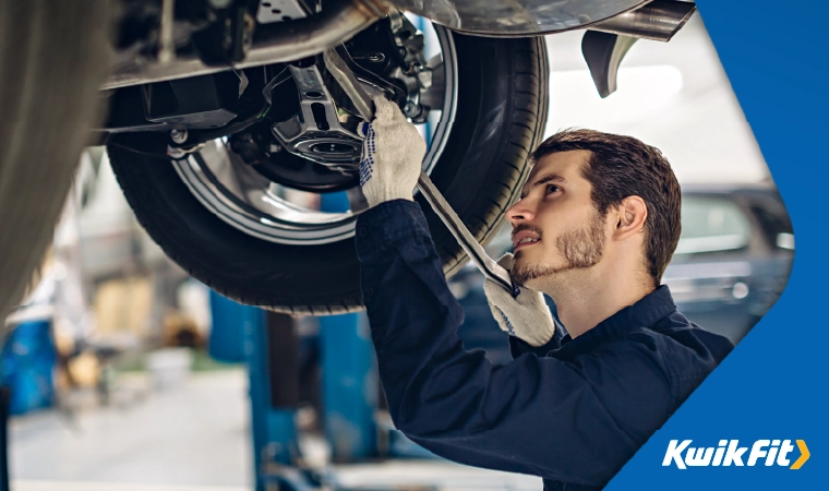 Technician in blue boiler suit checking the underneath of a vehicle.