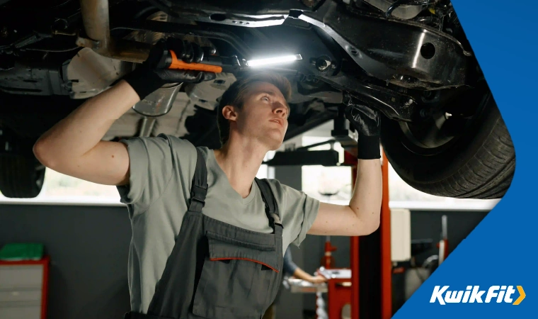 A mechanic checking the brakes and calipers of a vehicle with a flashlight.