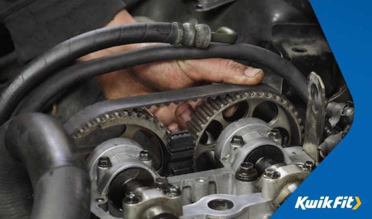 A hand holds a cambelt in place on the crankshaft.