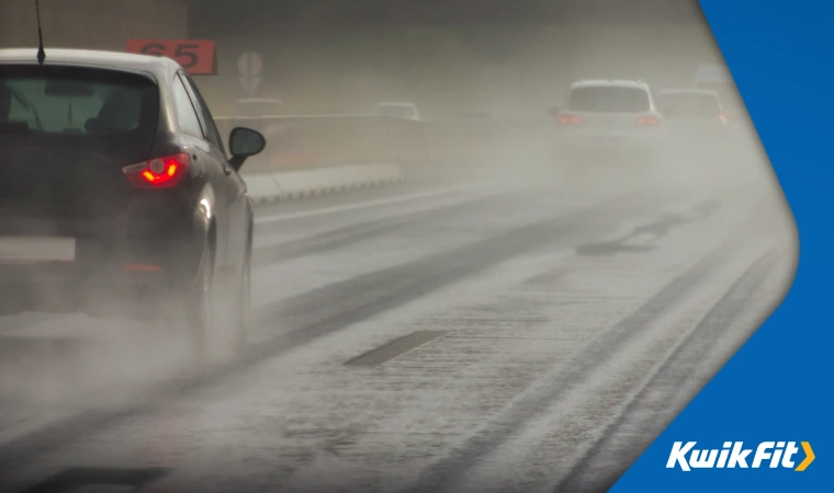 On a motorway in icy & rainy weather, spray being kicked up by car tyres.